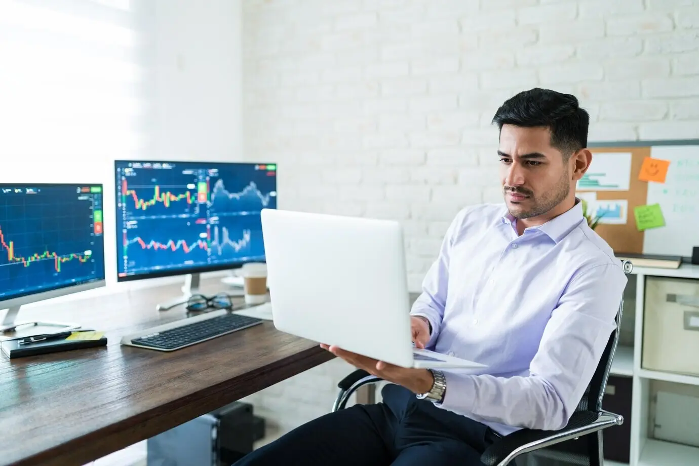 Привлекательный молодой трейдер-фрилансер использует ноутбук для торговли, работая из дома.